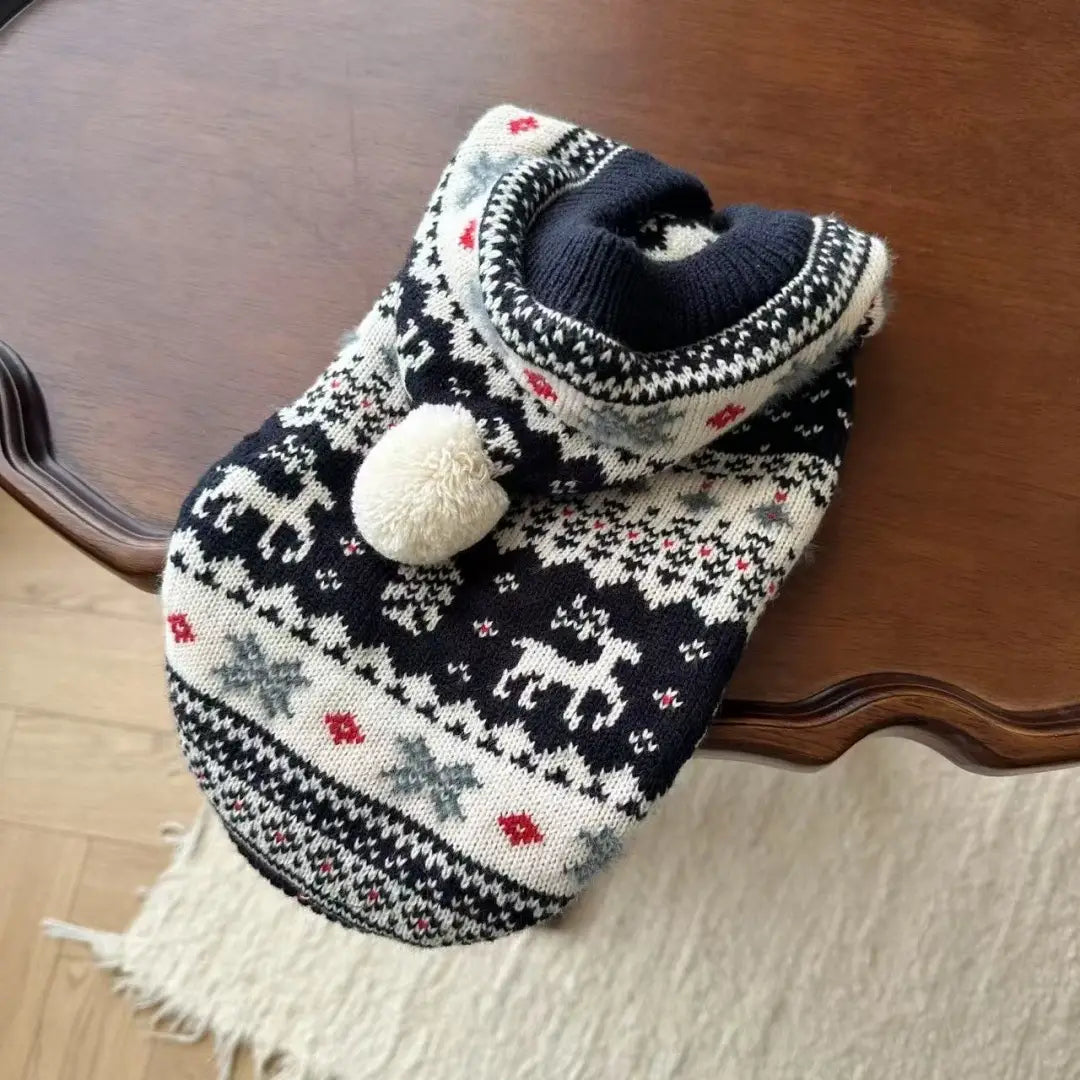 Pull en tricot nordique pour chien noir et blanc, avec des motifs de rennes et de flocons de neige, des accents rouges et un pompon crème duveteux sur la capuche, conçu pour des vêtements d’hiver chauds pour animaux de compagnie.