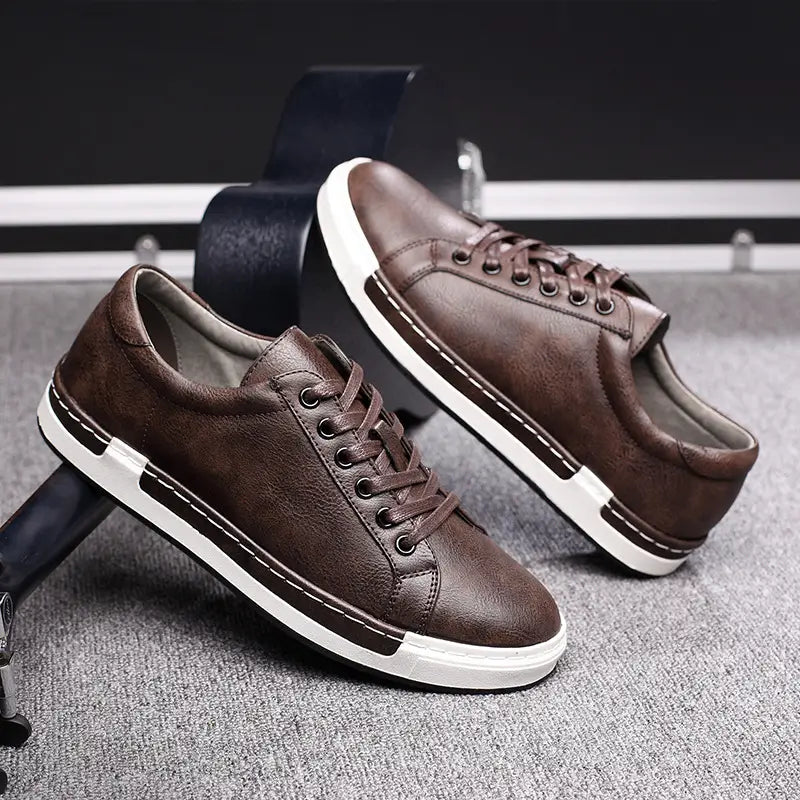 Les baskets basses en cuir pour homme, faites à la main, de couleur marron, avec un design à lacets, des semelles en caoutchouc blanc et des coutures contrastantes, pour un usage décontracté.