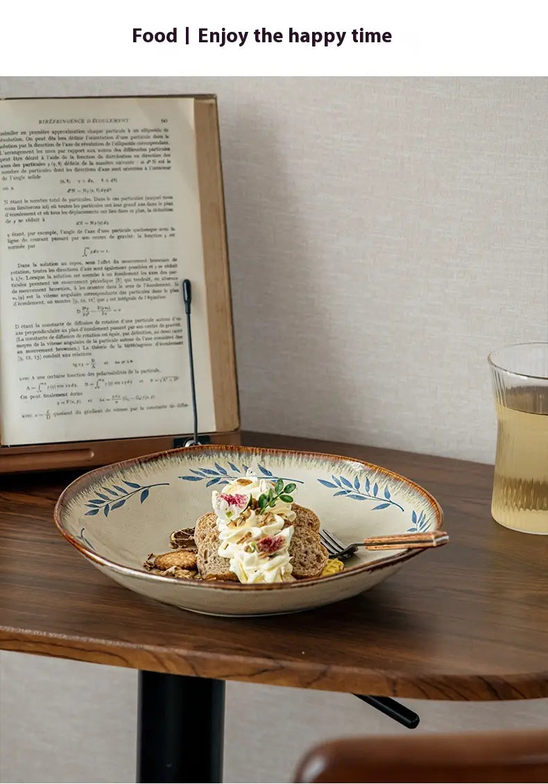 A 9-inch ceramic deep plate with a beige base and blue leaf pattern showing a slice of bread topped with cream cheese figs and herbs.