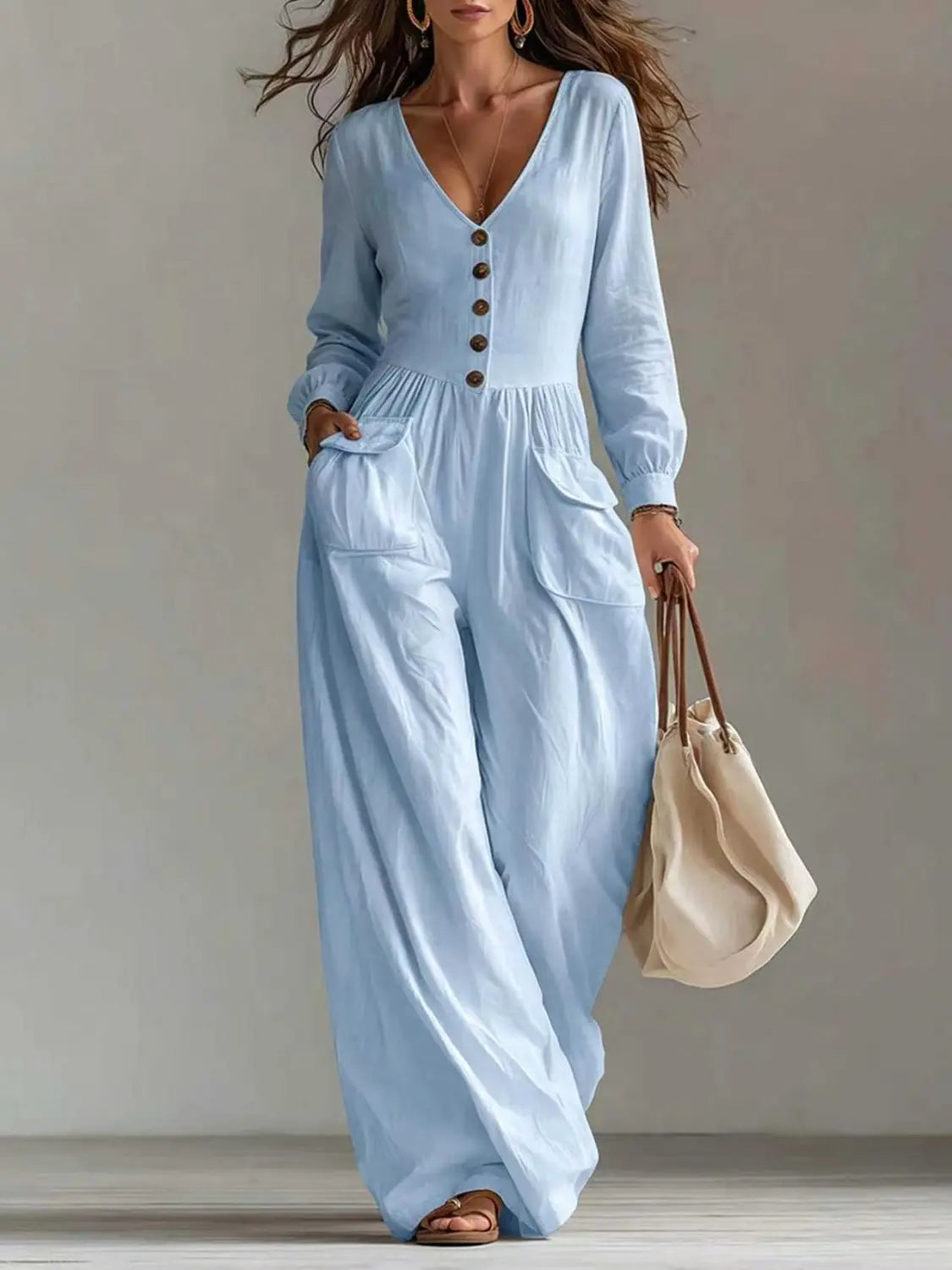 Une combinaison ample à jambes larges pour femmes bleu clair, décolleté en V, manches longues, avec détails à l’avant boutonné et tissu souple adapté à un usage décontracté ou formel.