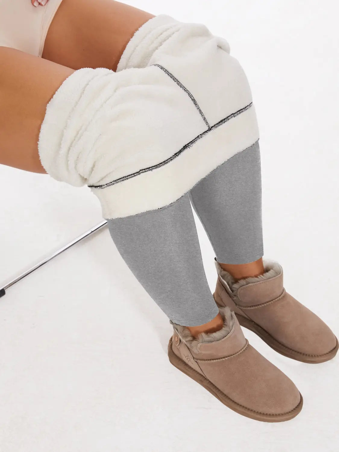 Beige suede ugg-style boots with plush fur lining and a simple buckle strap paired with fleece lined high waisted winter leggings.