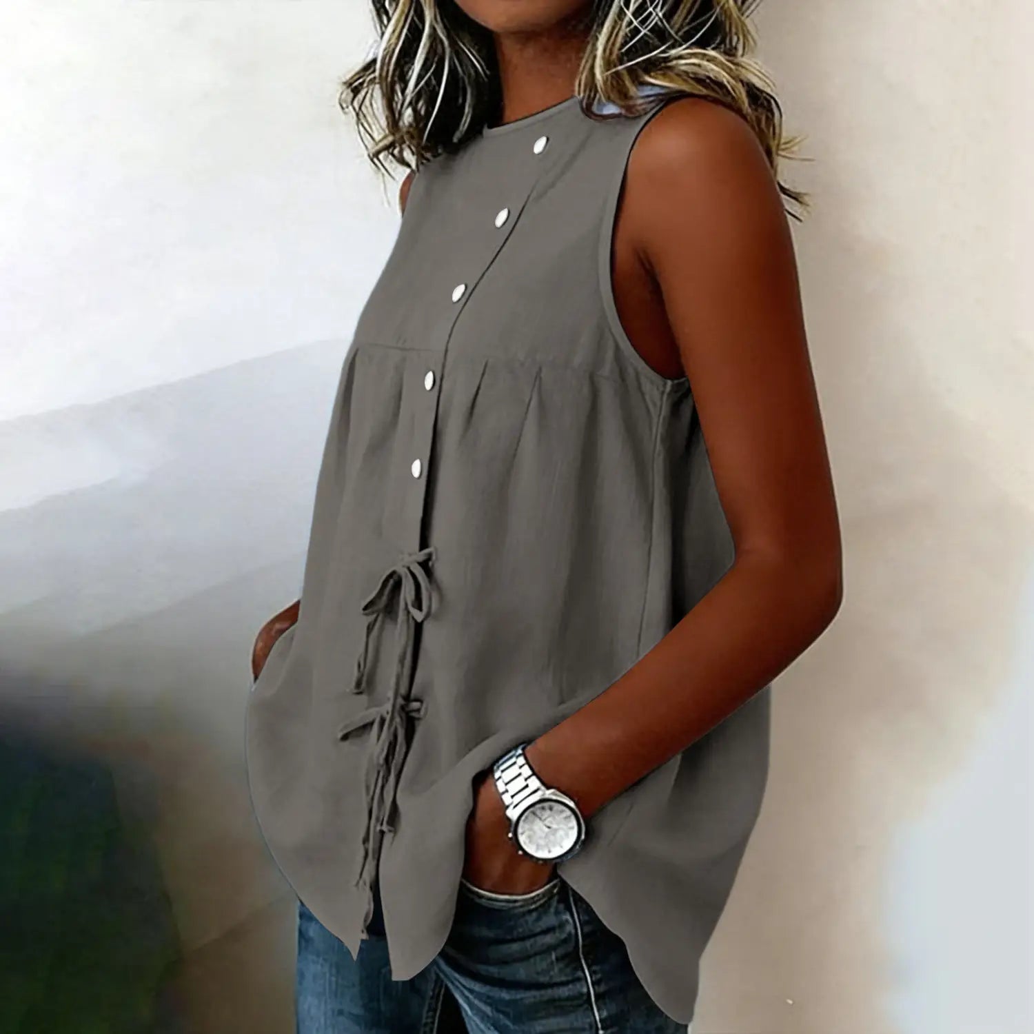 Gray sleeveless tie side button down blouse featuring white buttons down the front and a tied waist detail.