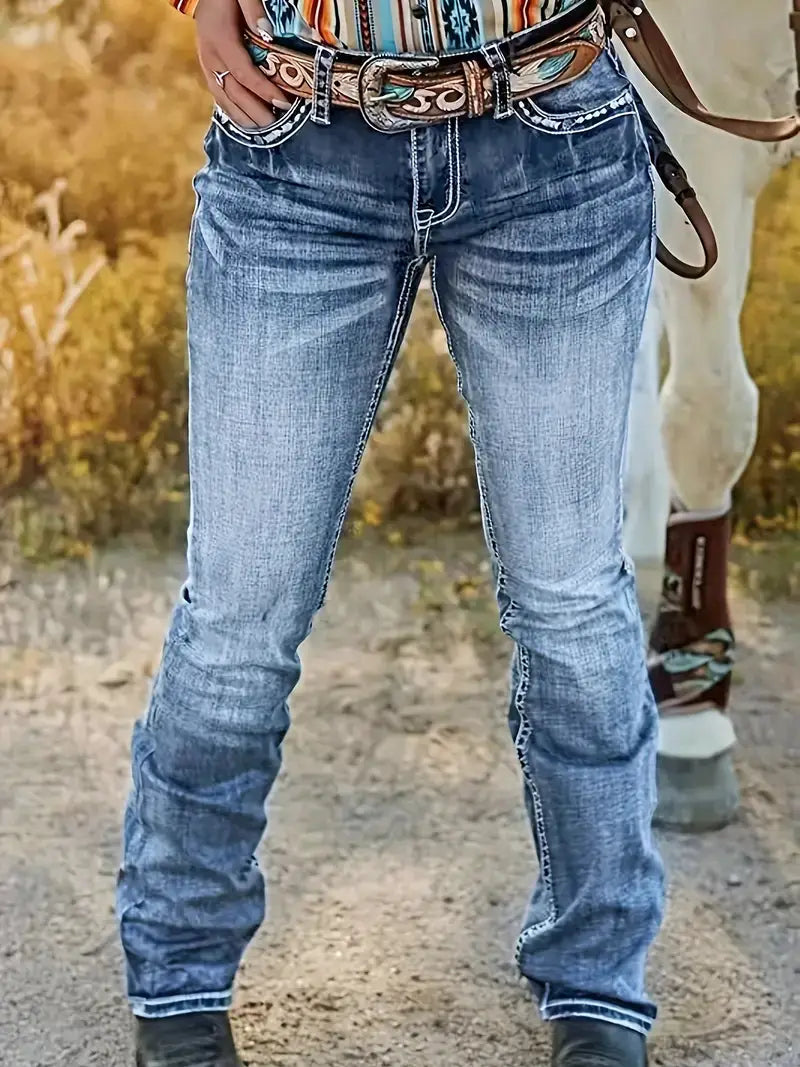 Jeans droits en denim brodé bleu à l’aspect délavé, avec surpiqûres blanches, associés à une ceinture ornée présentant des accents turquoise et bruns.