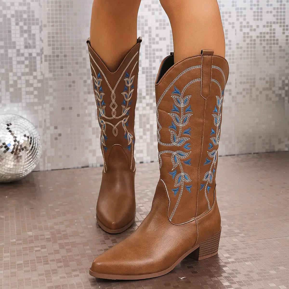 Brown leather western cowboy boots with blue and white embroidered floral patterns featuring a pointed toe and chunky heel.