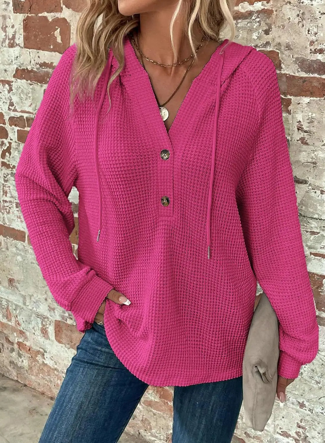 A vibrant pink women’s v neck waffle knit button hoodie sweater featuring a v-neck, three front buttons, and drawstrings.