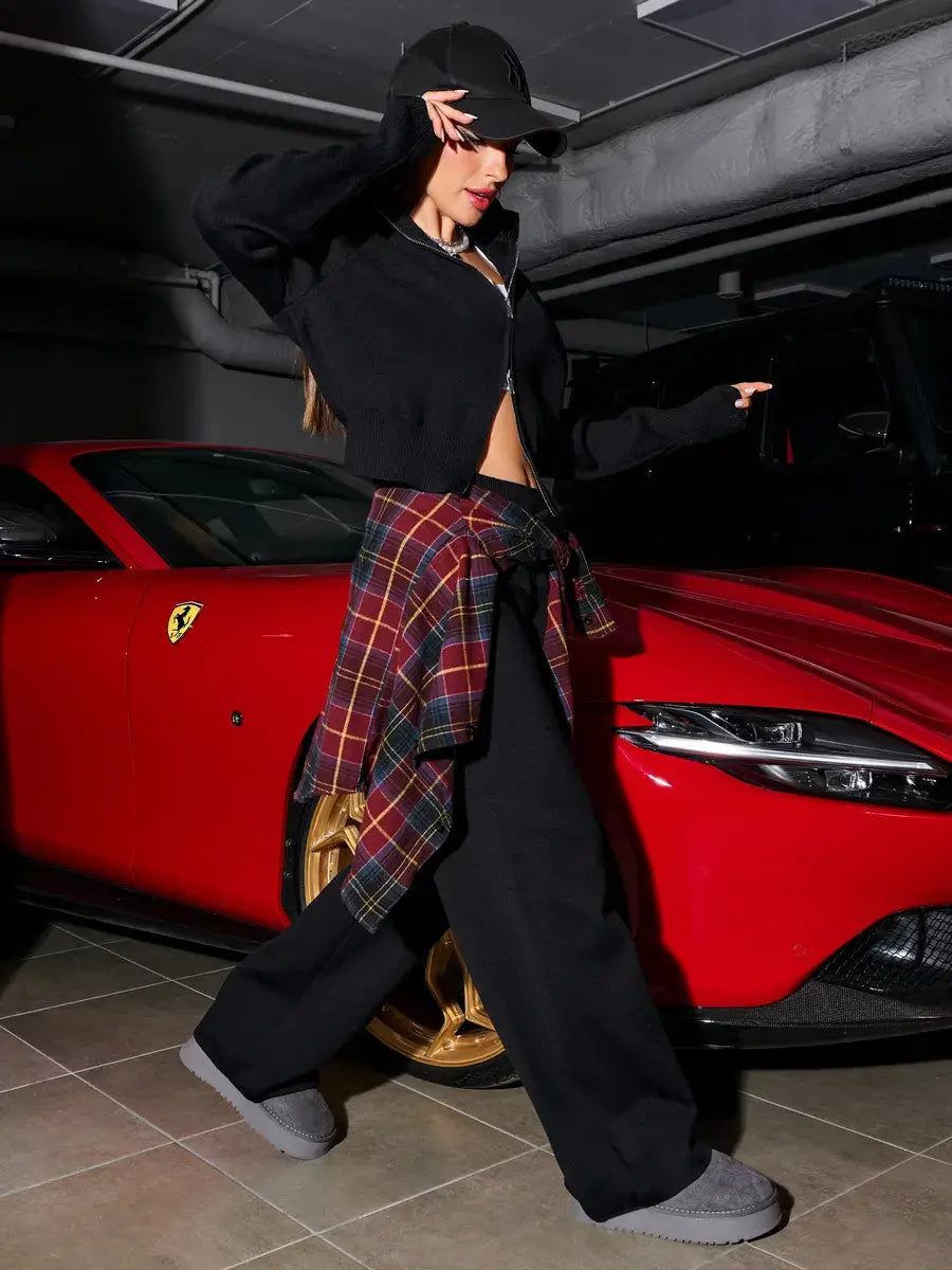 A red Ferrari sports car with gold-colored wheels and the prancing horse emblem is shown alongside a women’s knit zip up cardigan and wide leg pant set in neutral tones.