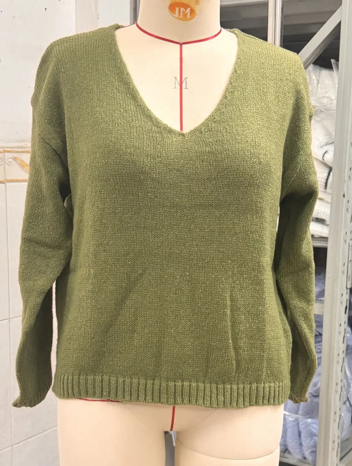 Olivgrüner Strickpullover mit V-Ausschnitt und überschnittener Schulterpartie, mit geripptem Saum aus weichem Strickmaterial.