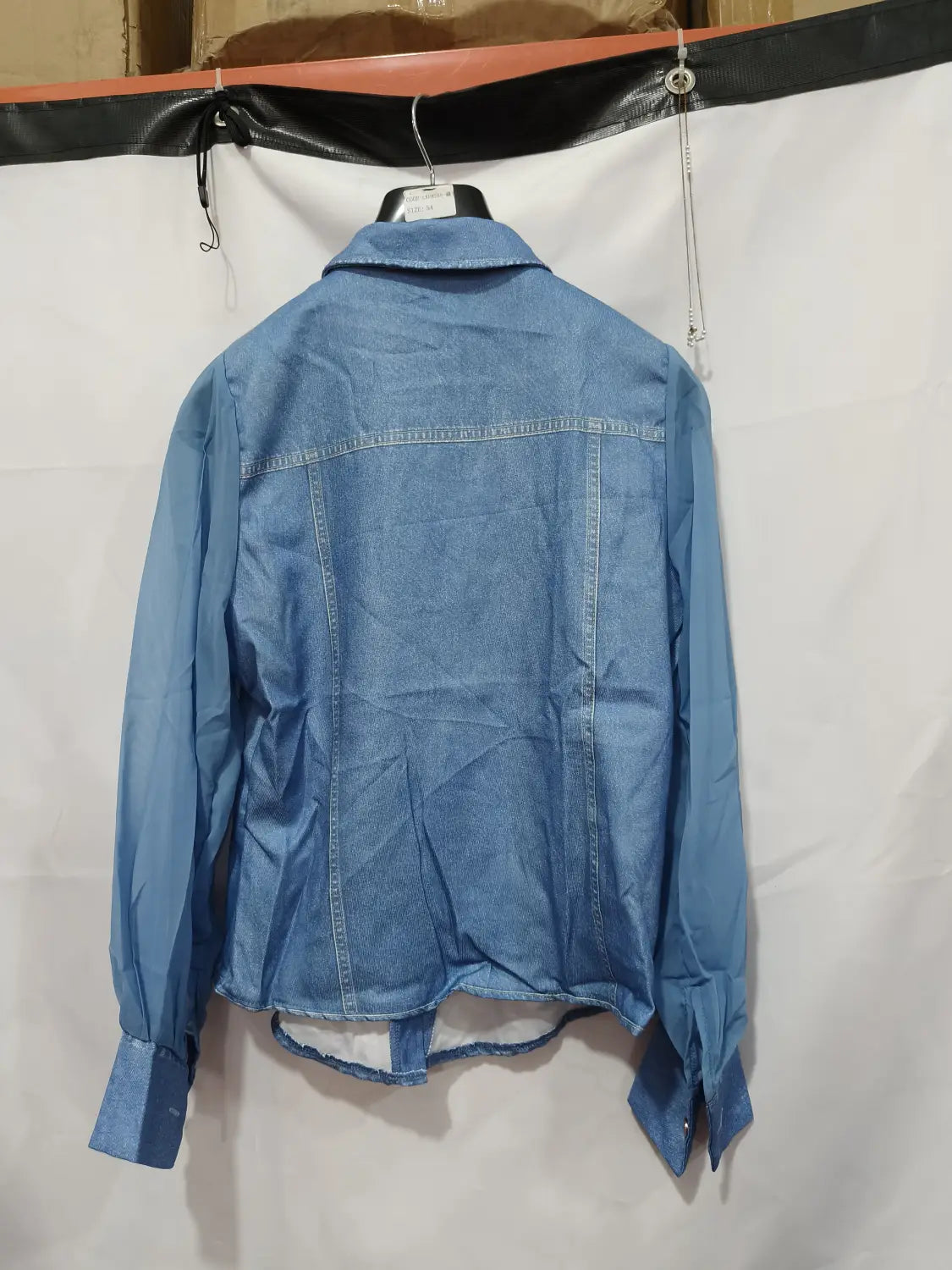 Un haut à encolure en V à manches transparentes en denim bleu clair, avec col classique et poignets boutonnés, suspendu à un cintre