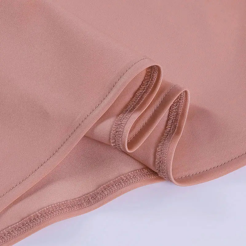 A soft peach-colored satin halter mini party dress fabric with a smooth slightly glossy texture and neatly stitched edges.