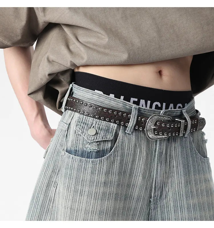 Dark brown leather belt with silver toned studs and an ornate buckle paired with striped denim capri shorts.