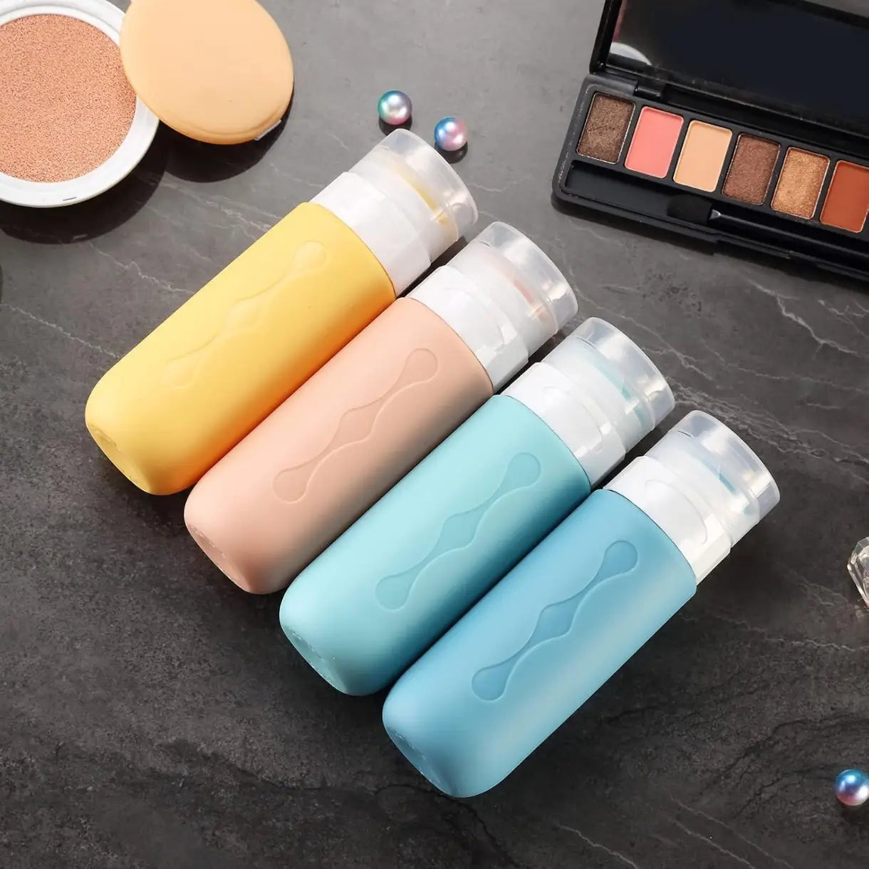 ensemble de quatre flacons de voyage en silicone réutilisables colorés, avec des bouchons transparents à vis et des prises texturées ondulées, conçu pour un usage anti-fuite.