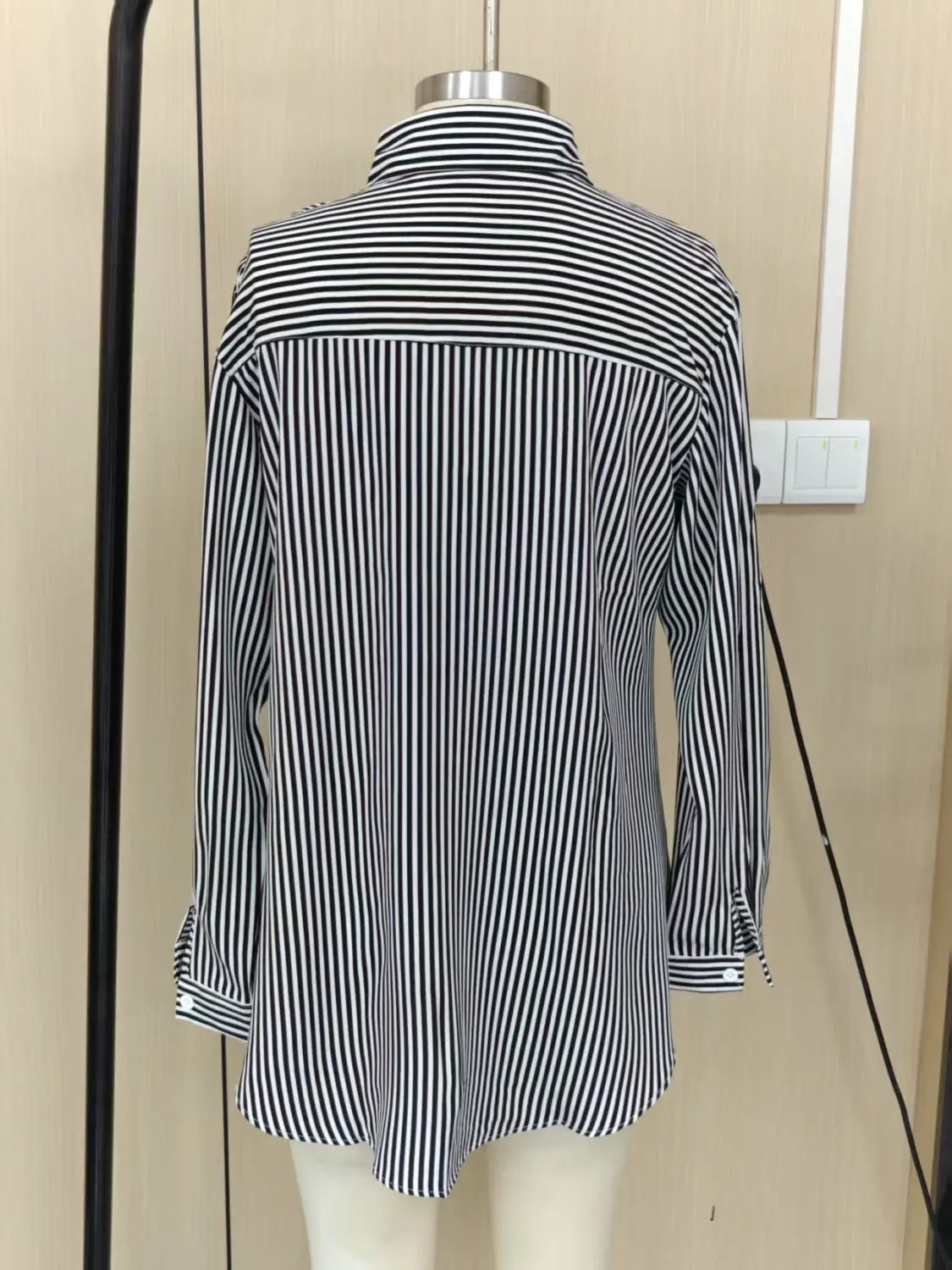 Chemise boutonnée à rayures verticales noir et blanc à manches longues avec col, adaptée à un usage décontracté.