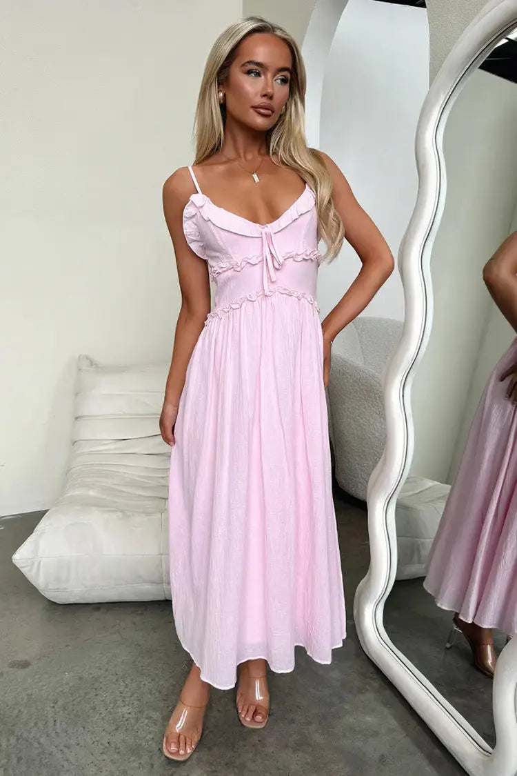 A soft pink flowing maxi vacation dress with delicate ruffled sleeveless straps and a gathered waistline.