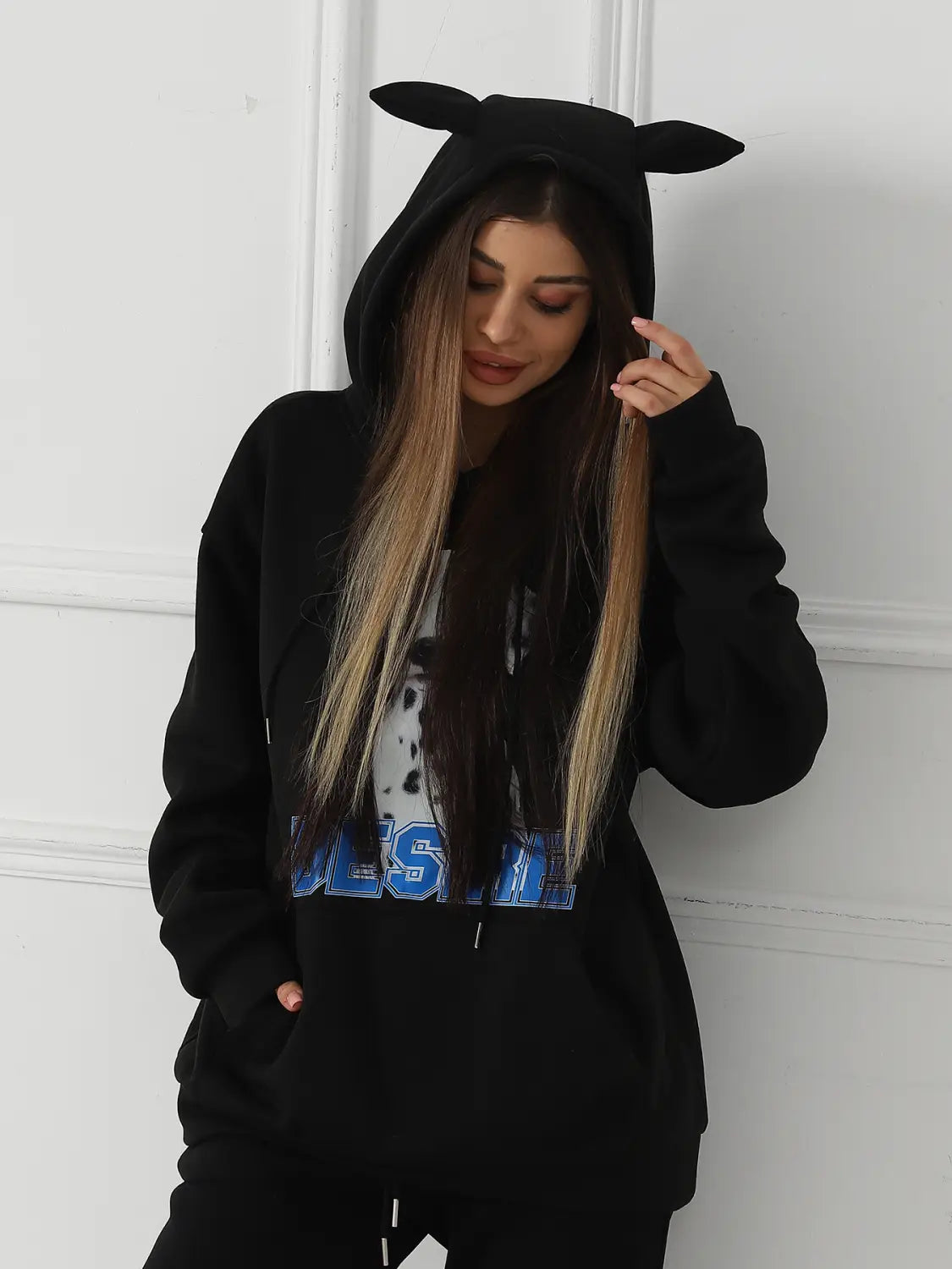 Black women’s hoodie made of soft fabric featuring a dalmatian print with cat ear trim on the hood and a graphic print across the chest.