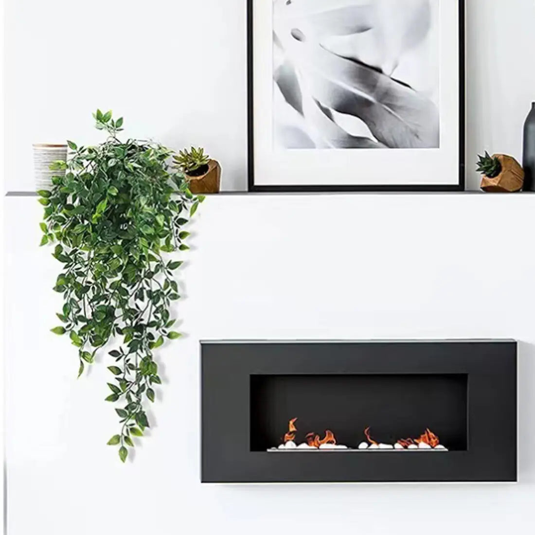 black rectangular electric fireplace with glowing orange flames and white pebbles inside displayed alongside artificial hanging plants 3 pack fake trailing greenery