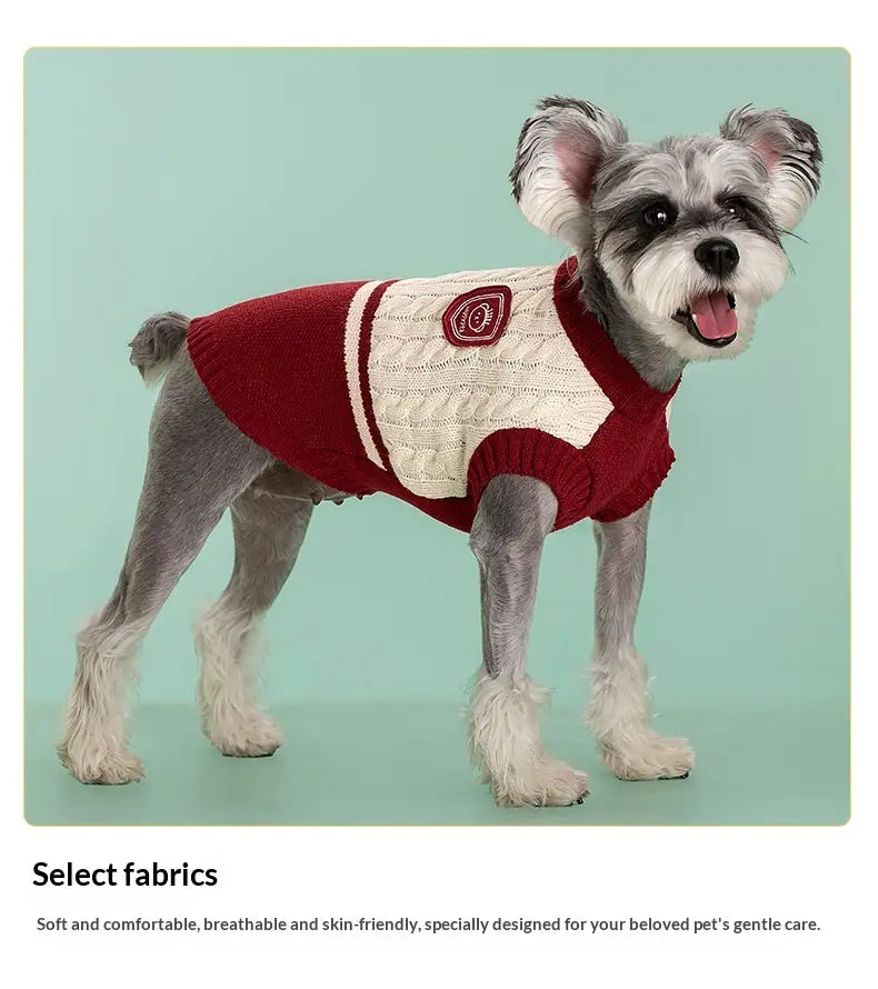 Ein gemütlicher roter und cremefarbener Zopfmuster-Hundepullover aus warmem Strickmaterial mit weißen Streifen an den Ärmeln und einem kleinen bestickten Aufnäher auf der Rückseite.