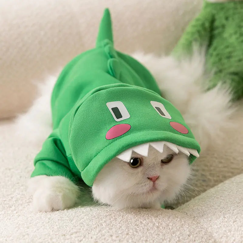 a fluffy white cat wearing a green dinosaur cat hoodie plush pet costume with pink cheeks and white teeth
