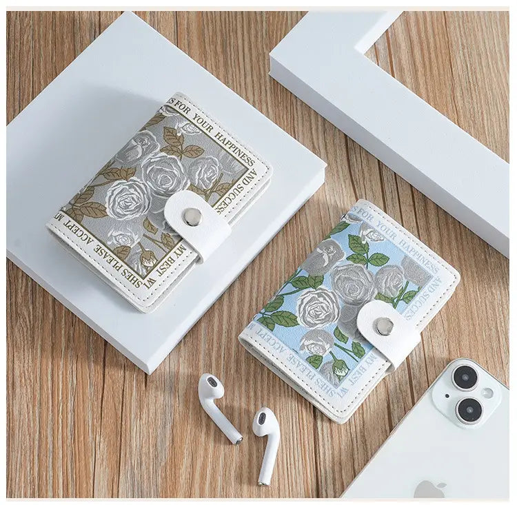 Two floral-patterned vintage floral pu leather multi slot card holder wallets in silver-gray with rose motifs and light blue, both featuring white leather-like straps and embossed inspirational phrases along their edges.