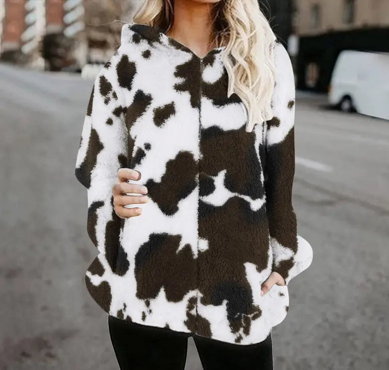 Una sudadera con capucha tipo zip-up de manga larga y estilo acogedor, confeccionada con una tela acolchada blanca y marrón con estampado de vaca, denominada chaqueta acolchada tipo zip-up con estampado de vaca.