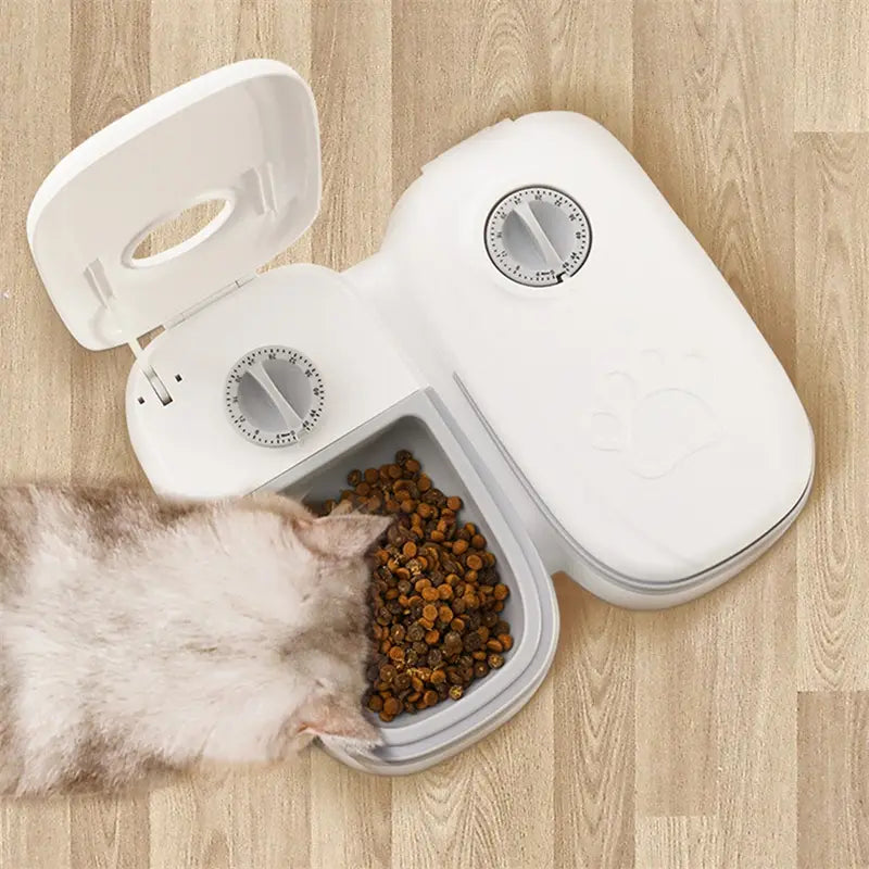 White plastic automatic pet feeder with two dial controls and gray food compartment filled with brown kibble for gravity waterer and food dispenser use.