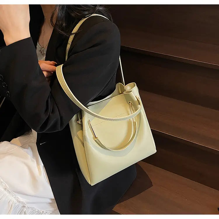 Cream-colored minimalist leather bucket bag with a top handle and detachable adjustable shoulder strap.