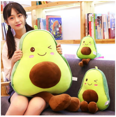A plush avocado-shaped soft fruit pillow for kids with a green body, brown pit, and embroidered facial features.