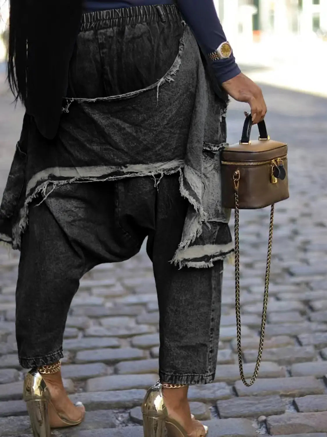 Braune Leder-Minihandtasche mit schwarzen Tragegriffen und einem goldfarbenen Kettenriemen, zusammen mit bestickten Patchwork-Jeans-Haremshosen dargestellt