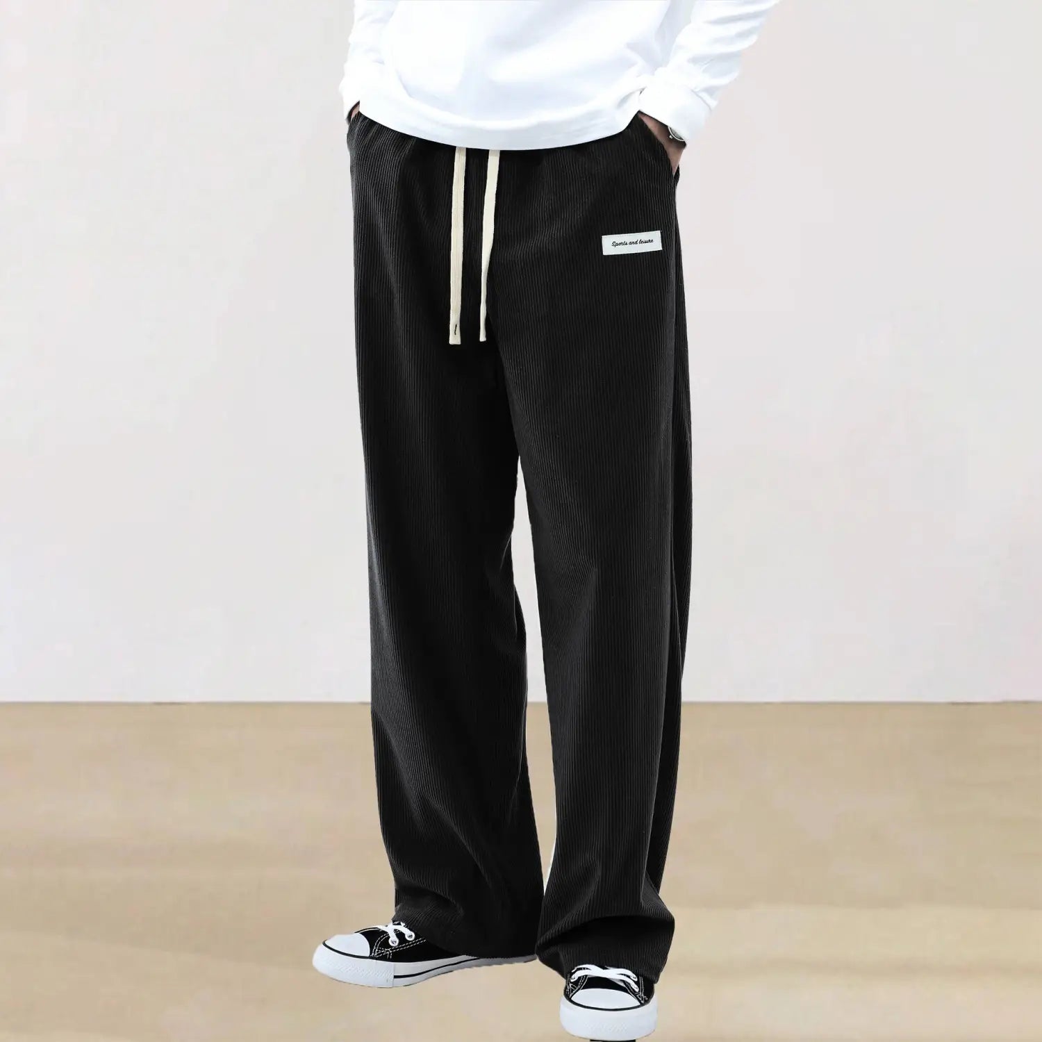 Men’s slim fit black corduroy casual pants with a relaxed fit, contrasting white drawstrings, and a small rectangular brand label on the upper right leg.