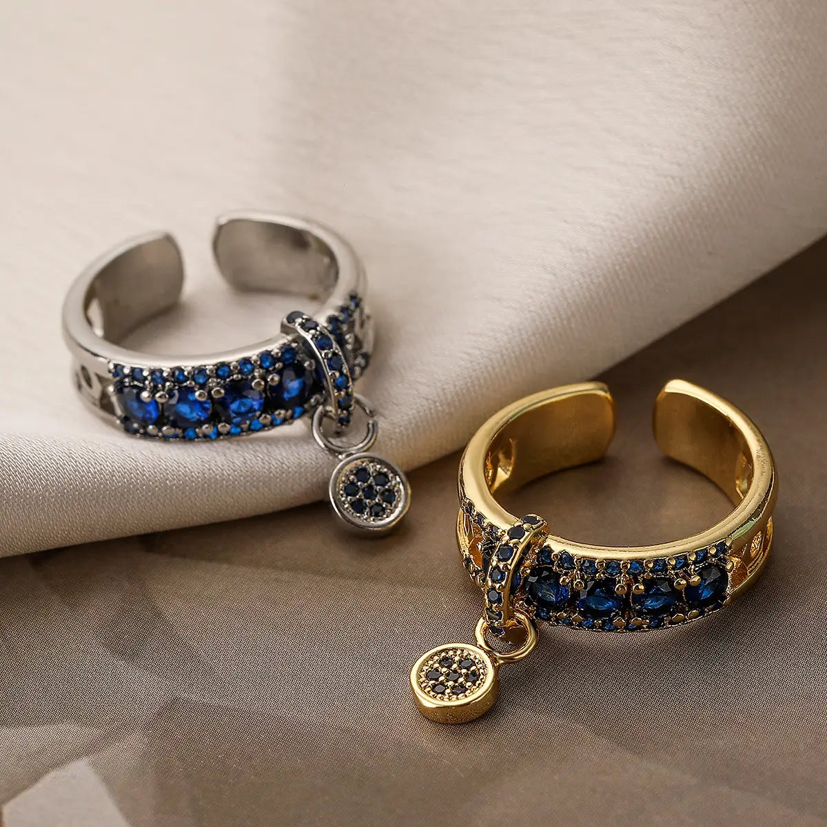 Two adjustable open-toe rings in gold and silver featuring blue zircon gemstones and matching dangling geometric charms.