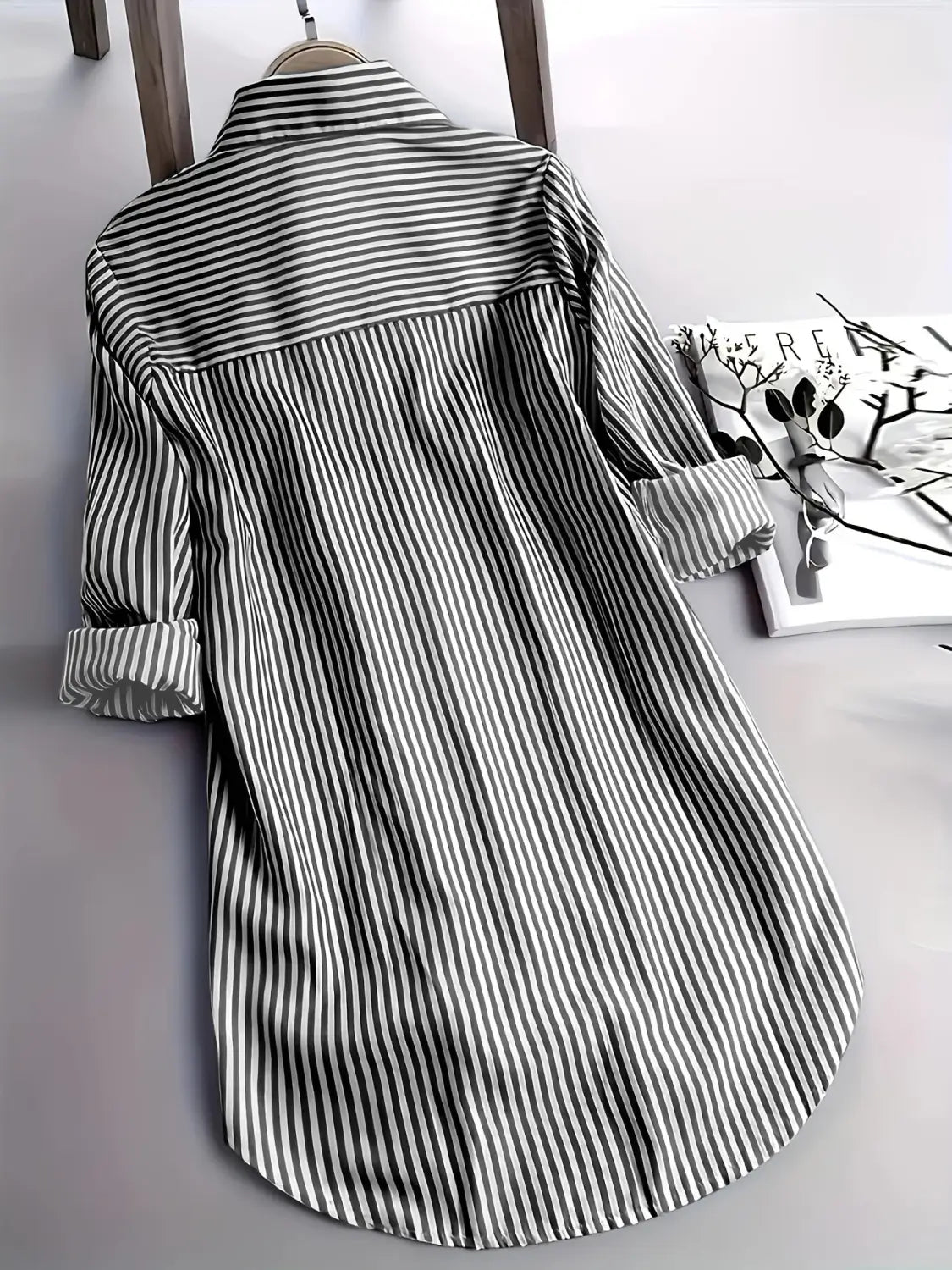 Chemise boutonnée à rayures verticales noir et blanc à manches longues avec col, présentée sur un cintre en bois, adaptée à un usage décontracté.