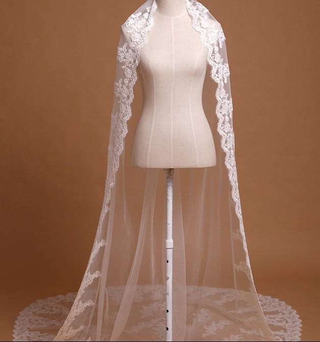 A delicate white lace cathedral wedding veil with intricate embroidered floral edges displayed on a mannequin.