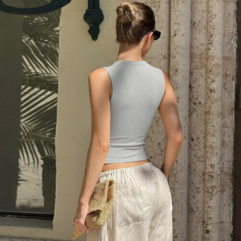 Top court sans manches côtelé gris clair avec détails de boutons, réalisé dans un tissu tricoté doux pour un usage décontracté.