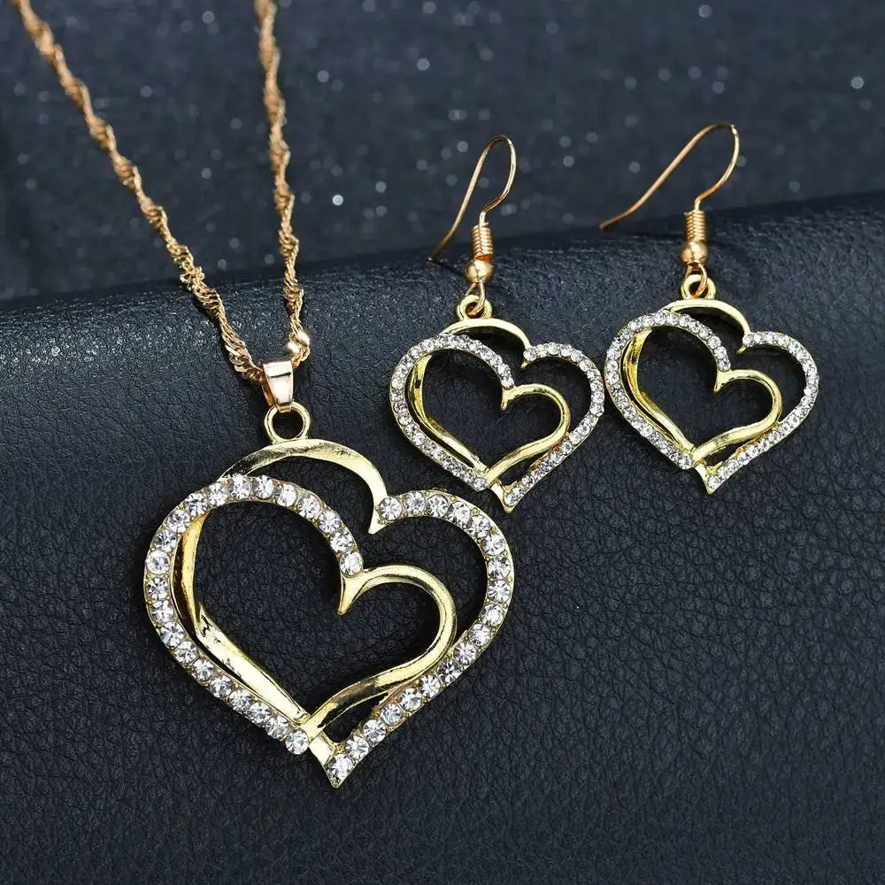 Elegant rhinestone heart jewelry set featuring a gold heart-shaped pendant necklace with a twisted rope chain and matching earrings adorned with clear rhinestones along the outer edges of interlocking hearts.