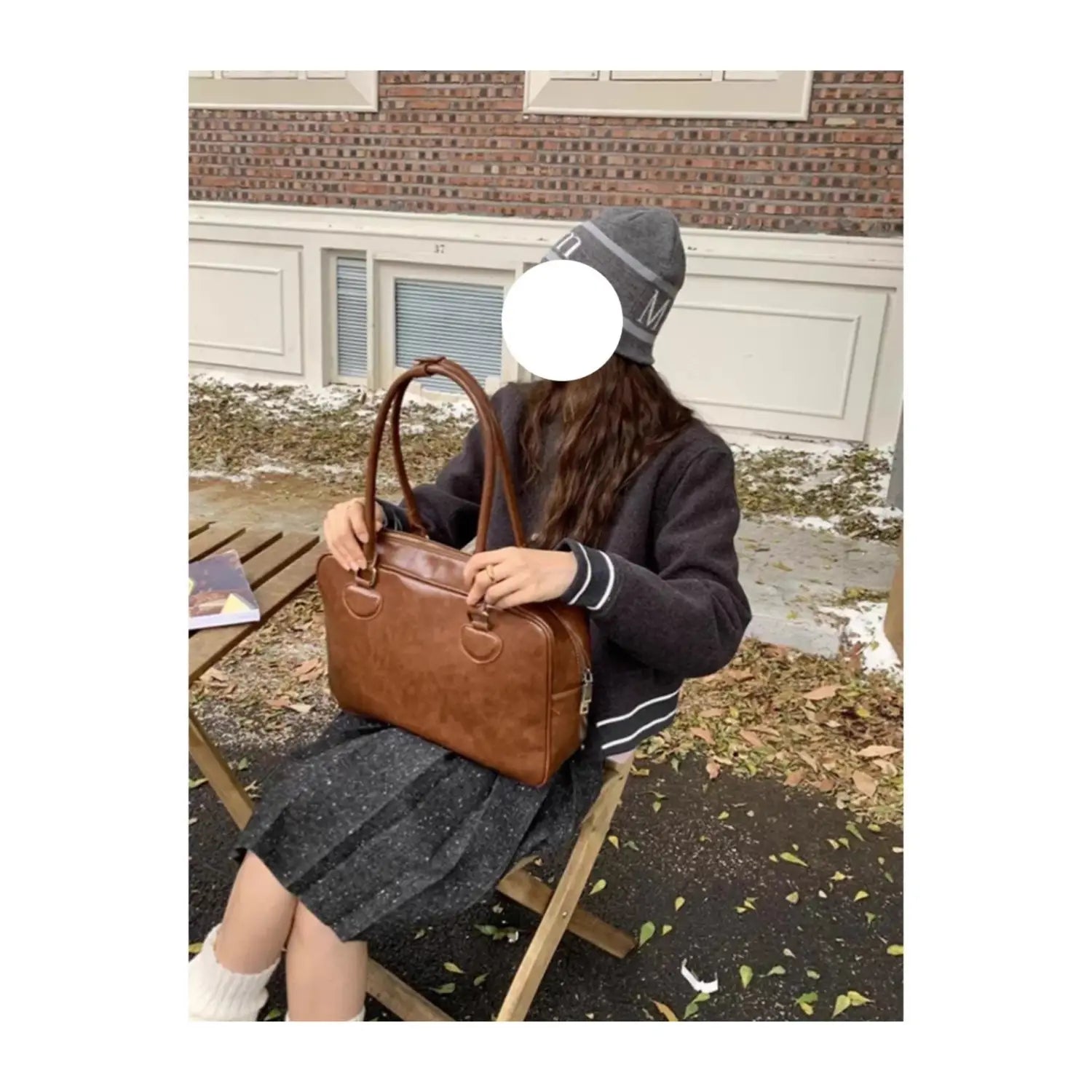 Brown leather satchel with large capacity, rounded top handles, structured rectangular shape, and bear charm for shoulder use.