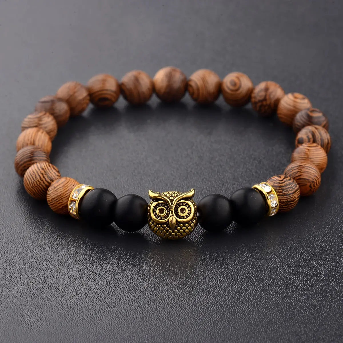 A gold-toned owl charm wood and onyx beaded bracelet featuring natural wood beads with swirling grain black onyx stones and small crystal accents.