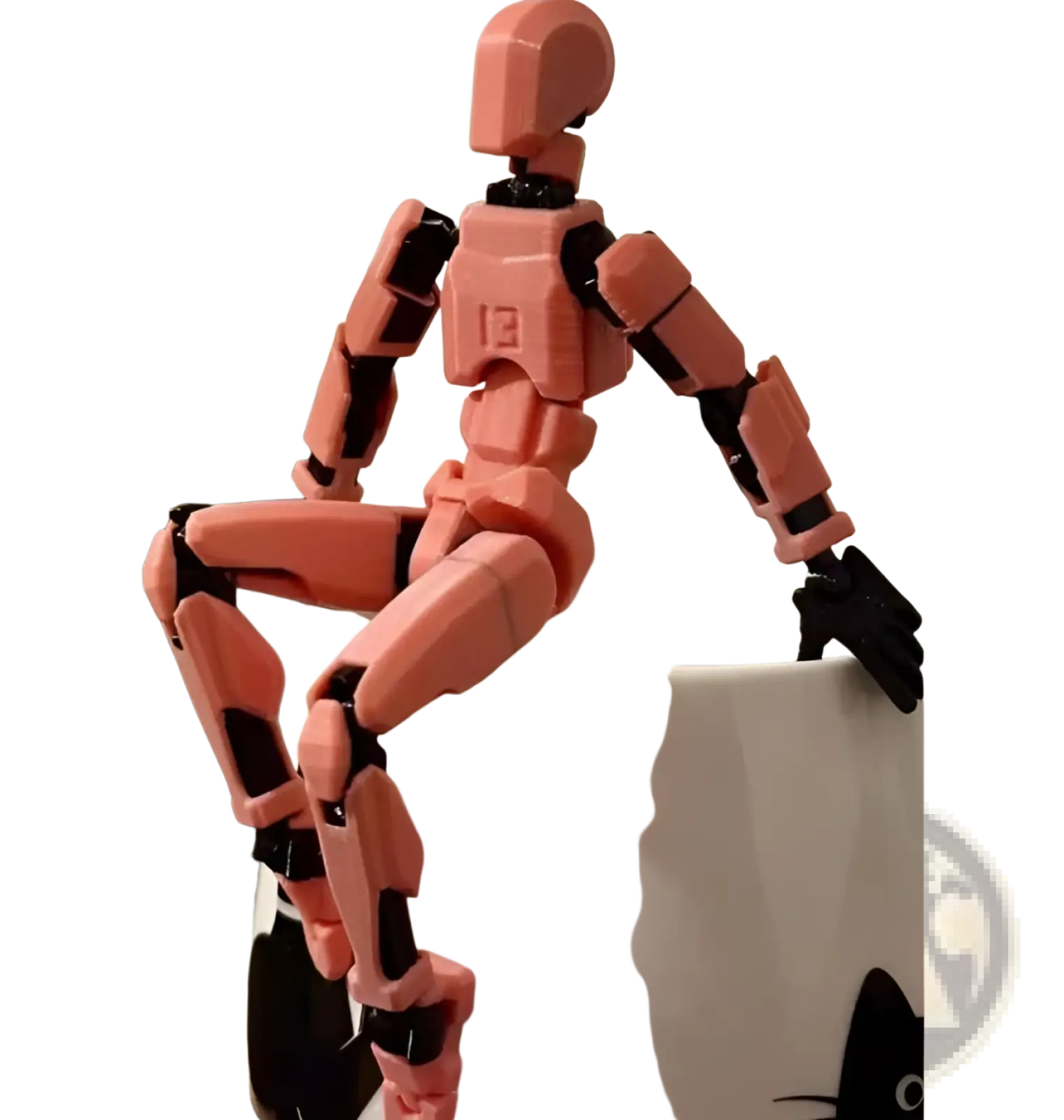 A pink and black 3d printed articulated robot action figure dummy 2.0 perched on the rim of a white mug