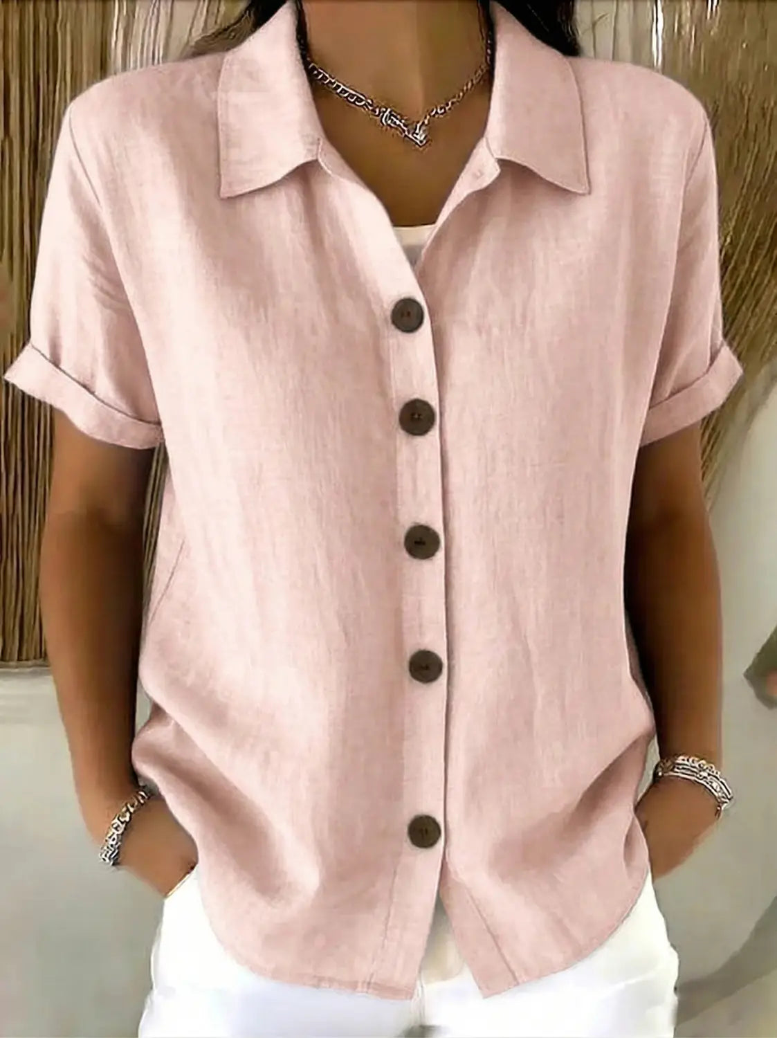Camisa de lino para mujer en rosa suave de manga corta con cuello y botones marrón oscuro, con puños enrollados.