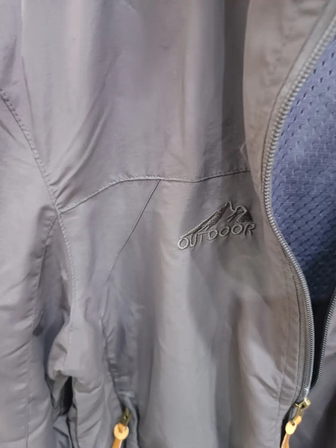 Chaqueta de senderismo con capucha impermeable color gris, con un logotipo bordado sutil en el pecho, diseñada para actividades al aire libre.
