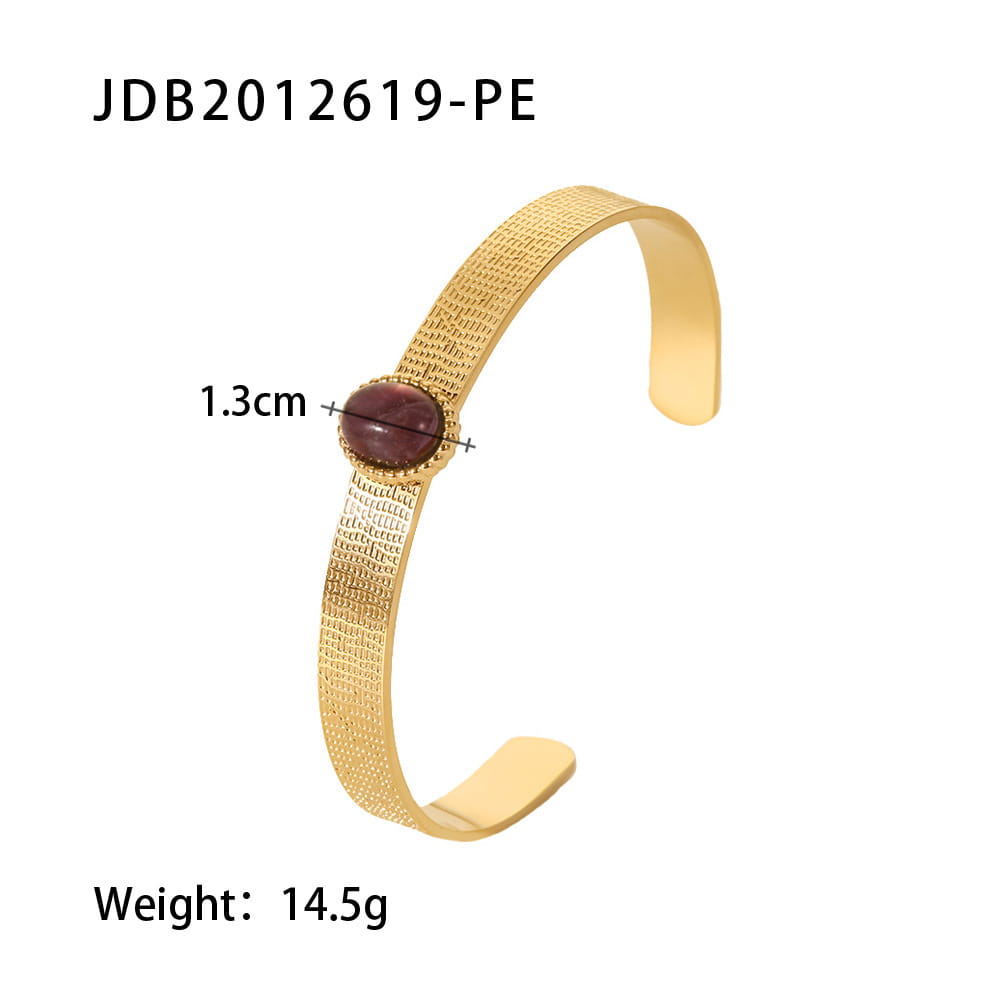 Gold plated stainless steel bangle bracelet with a gold-toned textured surface and an oval deep red zirconia gemstone set at the center.