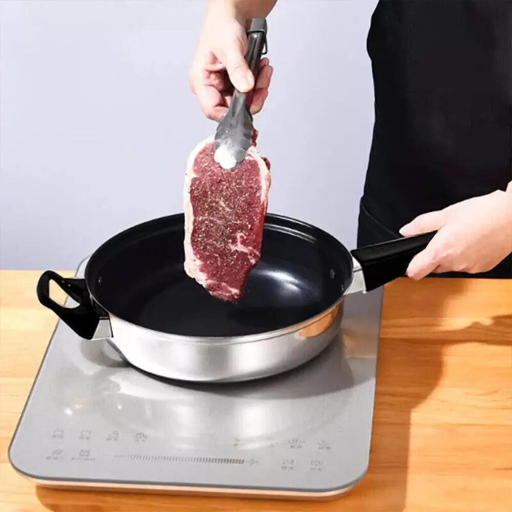 A thick marbled ribeye steak with a seasoned surface is held by metal tongs above a stainless steel frying pan from a 12 piece stainless steel cookware set with glass lids.