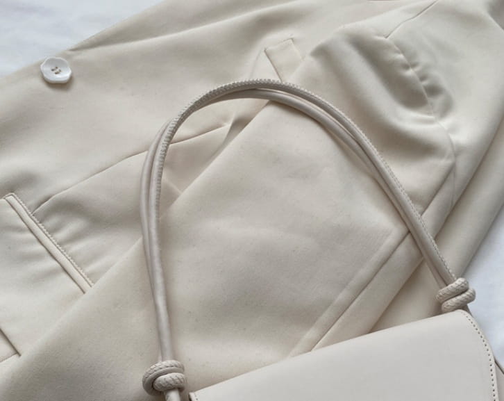 Cream-colored minimalist faux leather structured shoulder bag with braided rope handles and a simple design.