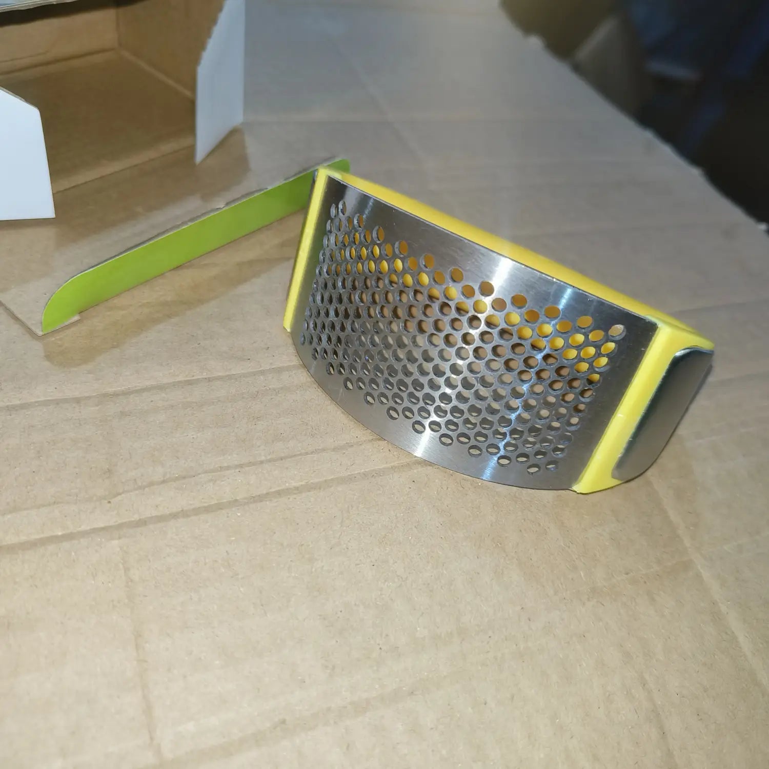Presse-ail jaune et en acier inoxydable, surface perforée en acier inoxydable conçue comme un outil de hachage manuel ergonomique.