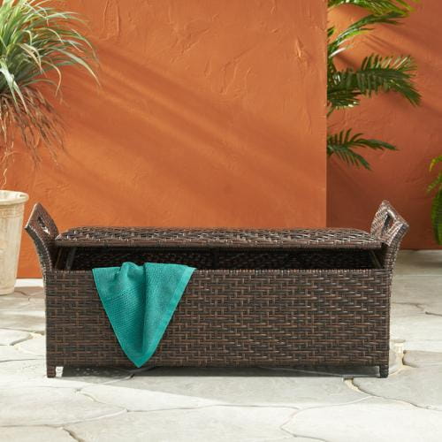 Brown wicker storage bench wing outdoor seating with a teal towel draped over its front.