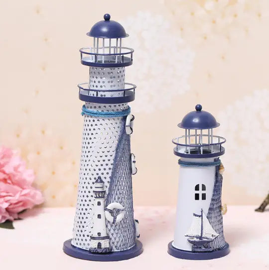 Two decorative metal Mediterranean lighthouse garden statue decor pieces featured with a taller white and navy blue perforated body with a small boat design and a shorter white solid base with a sailboat motif.