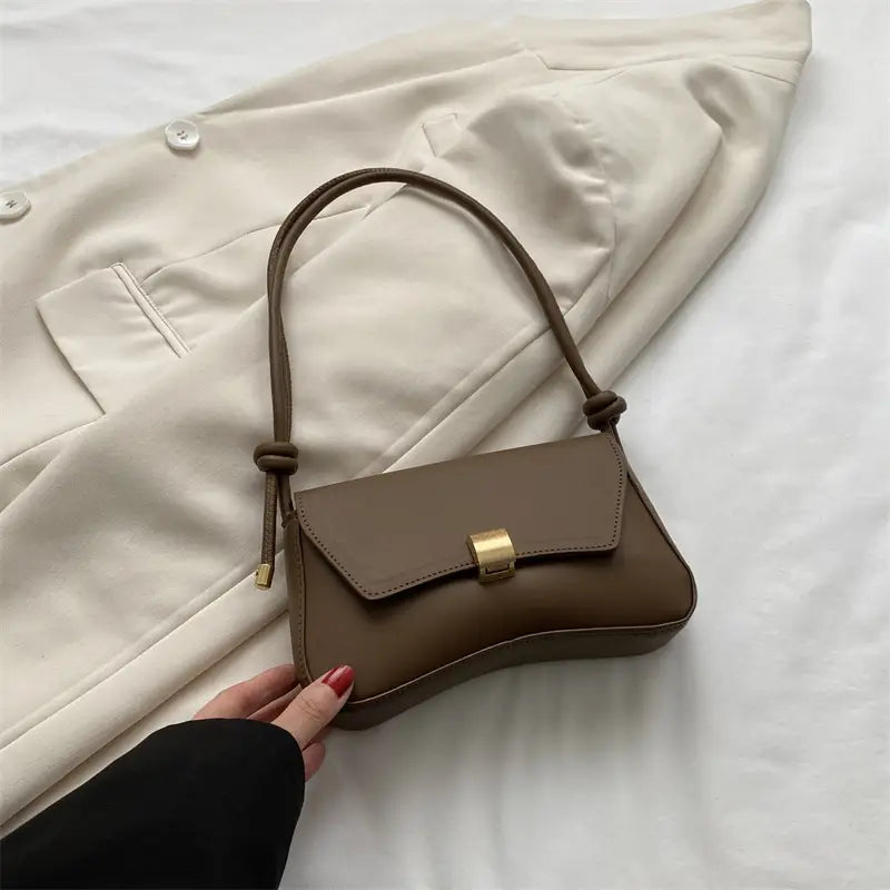 A minimalist taupe faux leather structured shoulder bag featuring a sleek design with a gold-tone rectangular clasp and a matching knotted shoulder strap.