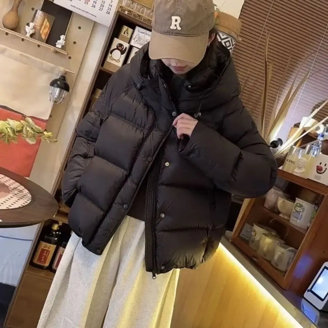 Chaqueta acolchada de plumón negra con capucha y cierre frontal con botones, diseñada para mujeres como una opción cálida de ropa exterior de invierno.