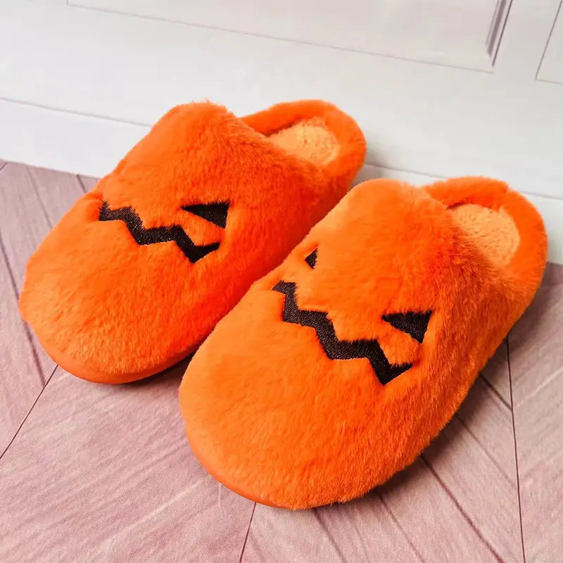 Plush pumpkin Halloween indoor slippers in orange with black embroidered facial features made from soft material.