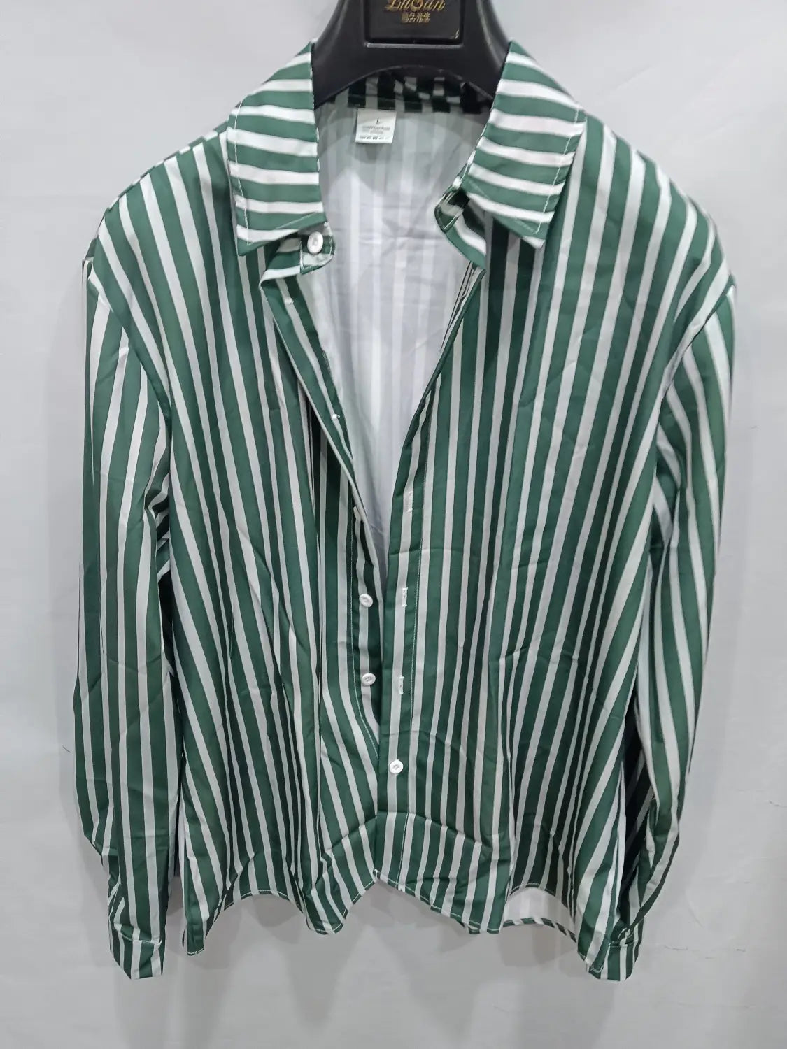 Chemise décontractée à manches longues rayée verticalement vert et blanc pour hommes, avec col et boutons, suspendue sur un cintre noir.