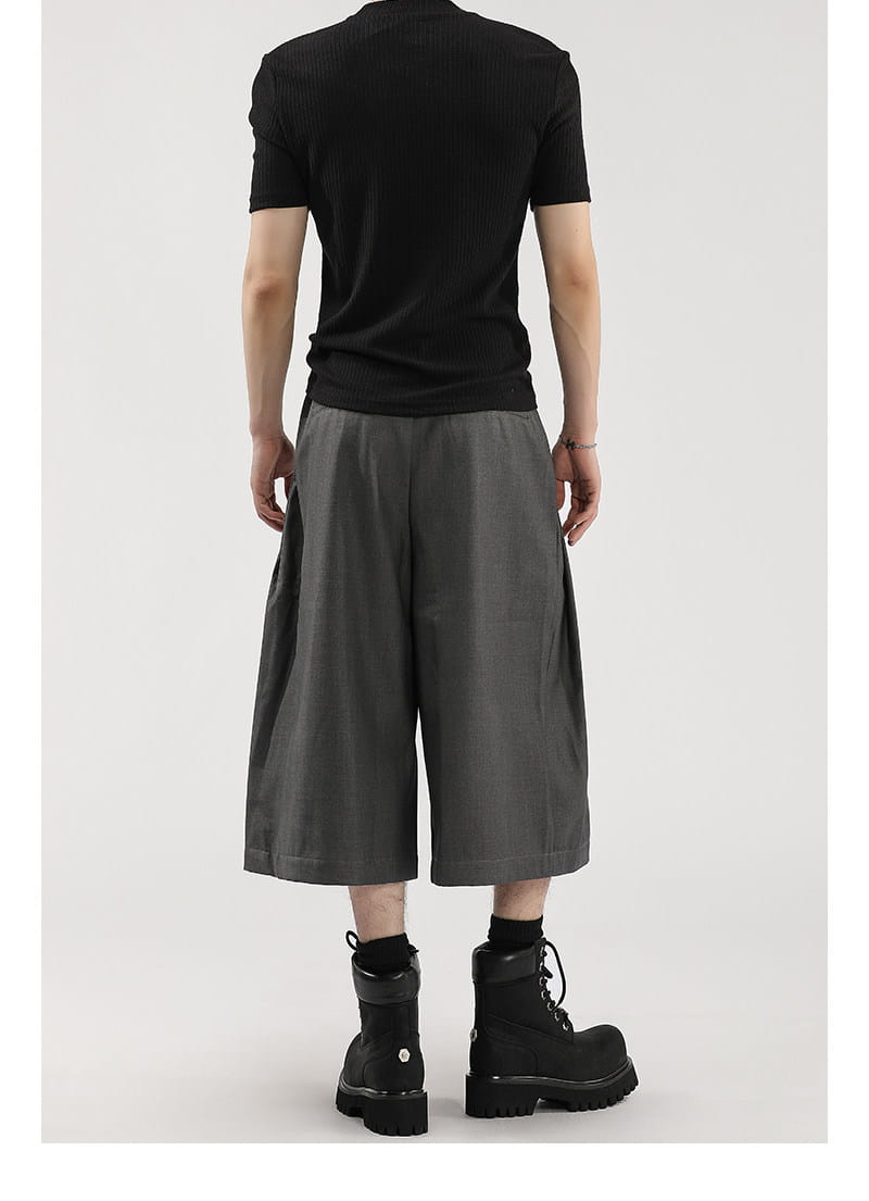 Short de costume pour hommes à jambes larges plissées gris charbon, associé à un haut noir à manches courtes côtelées et à des bottes de combat noires.