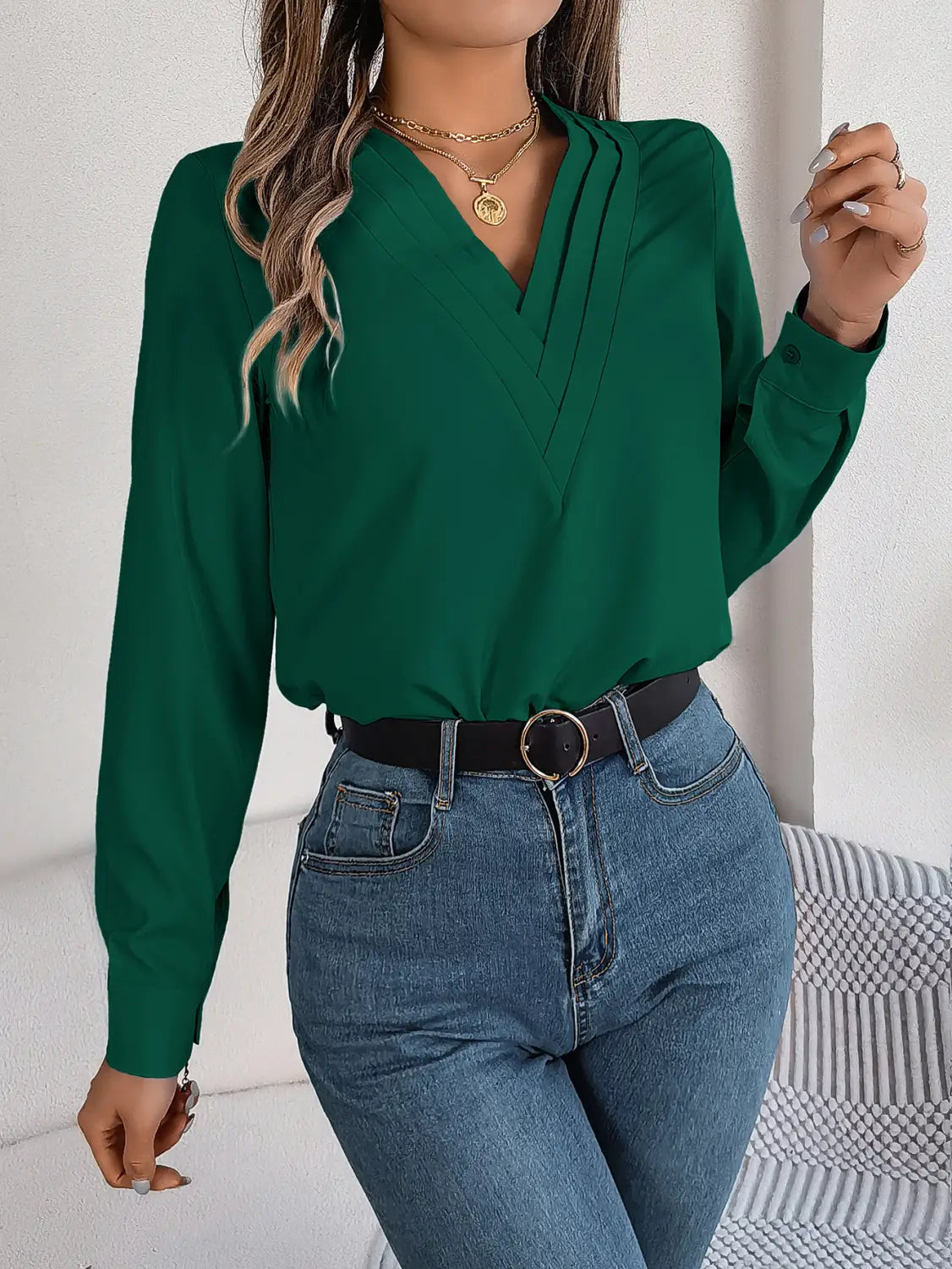 Emerald green long-sleeved blouse with a v-neck, subtle front pleats, and black trim designed as a white satin v neck wrap blouse.
